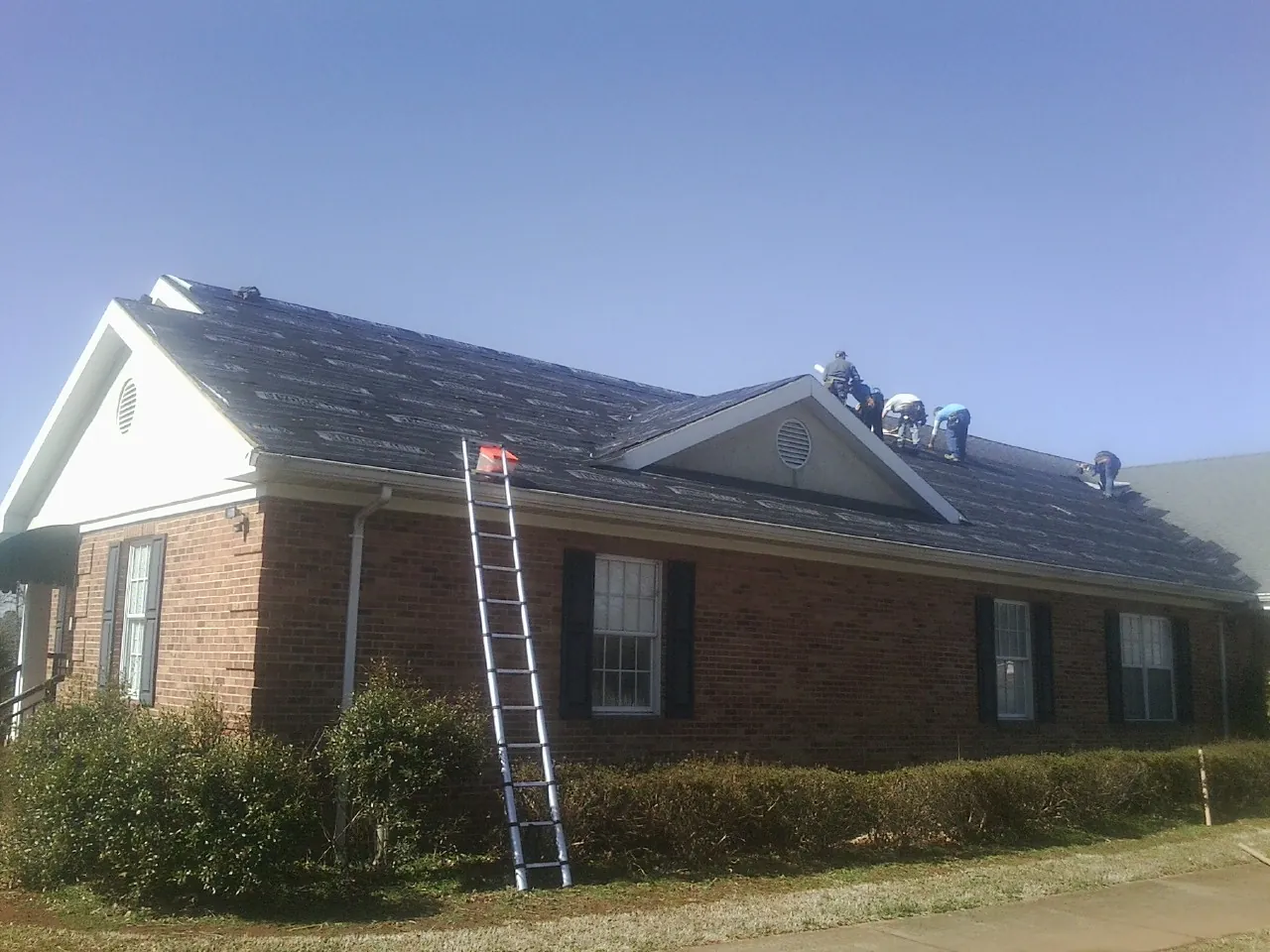 Crew tearing shingles off a brick ranch roof with a ladder set — Emergency Roof Repair work by our crew in Murphy