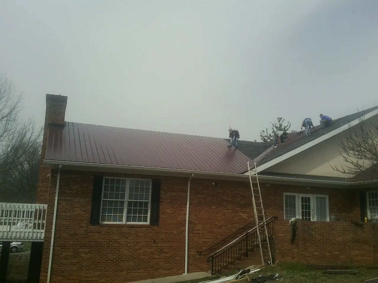 Crew setting red metal roofing panels on a brick home in Murphy