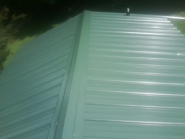 New green metal panels meeting at the ridge of a roof — Flat Roof Repair work by our crew in Murphy