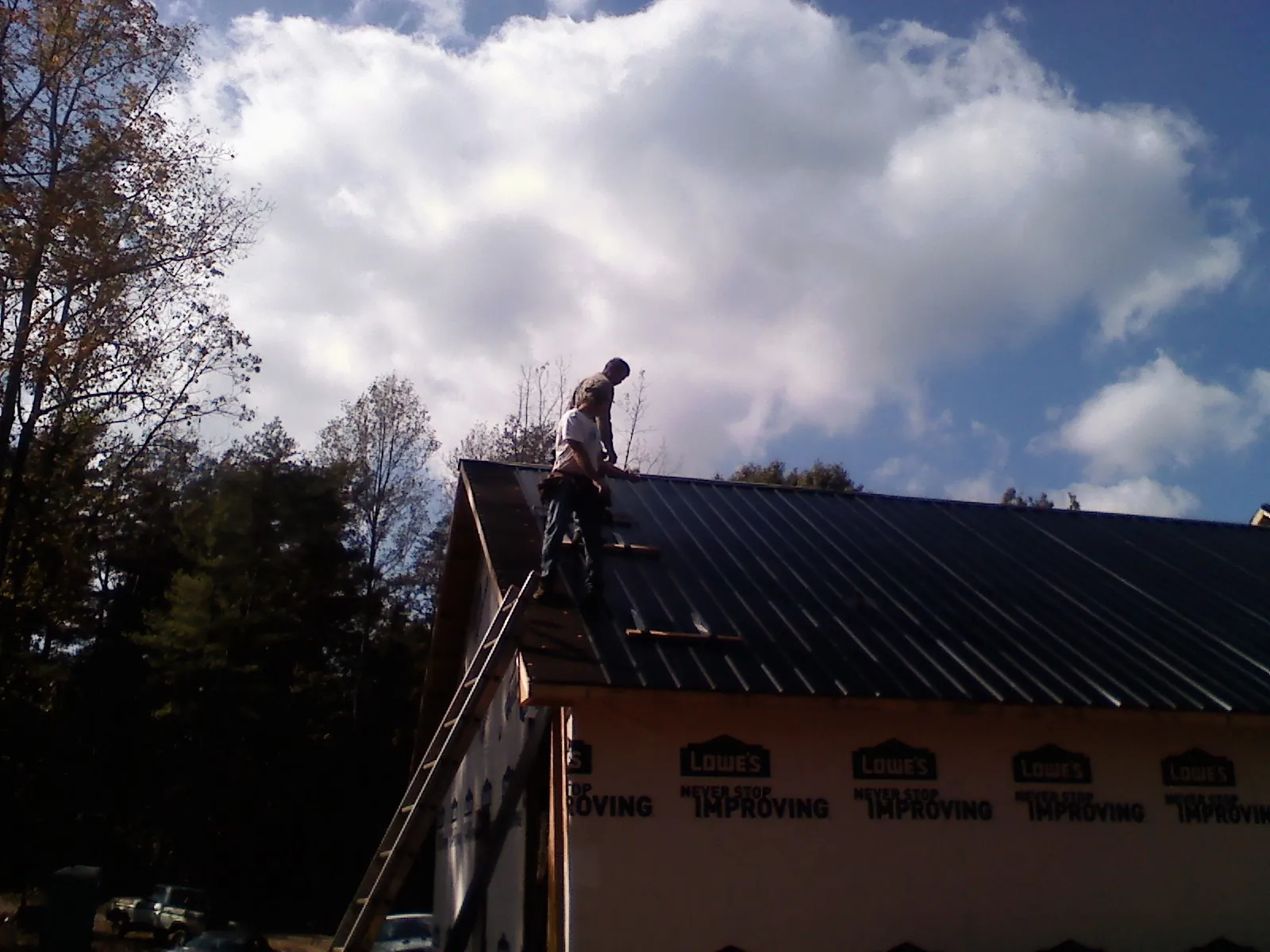 Roofer fastening dark metal panels high against a cloudy sky, from a Roof Inspection job in Murphy